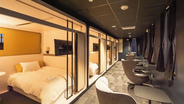 A hotel room with a bed, a desk, and a chair. There are curtains on the windows and a TV on the wall.