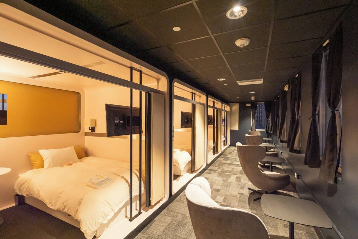 Ett hotellrum med en säng, ett skrivbord och en stol. Det finns gardiner vid fönstren och en tv på väggen.