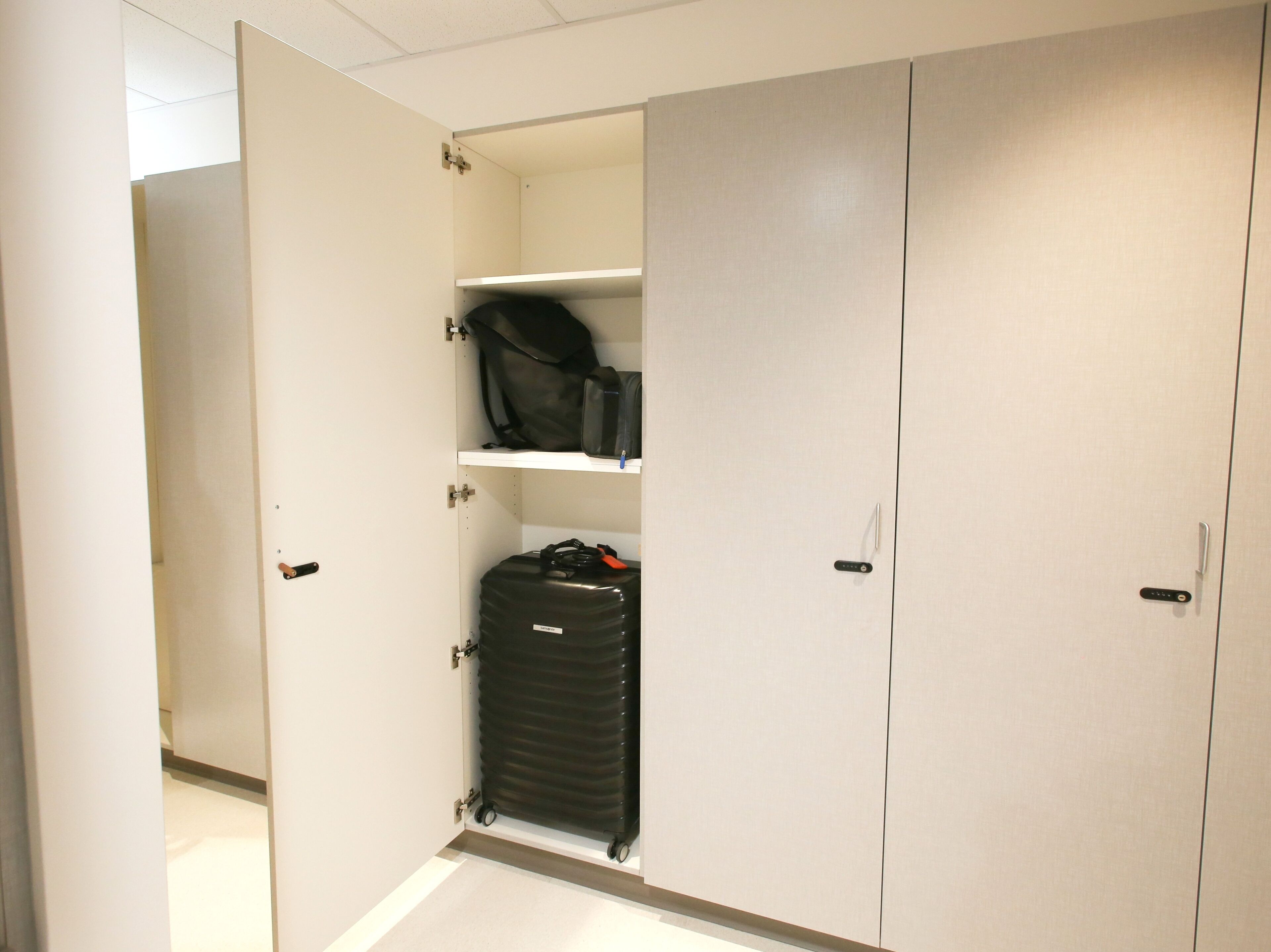 A walk-in closet with a large wardrobe, a shelf with a bag, and a wheeled suitcase.