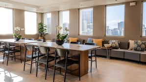 A spacious conference room with a long table, chairs, a sofa, and large windows offering city views.