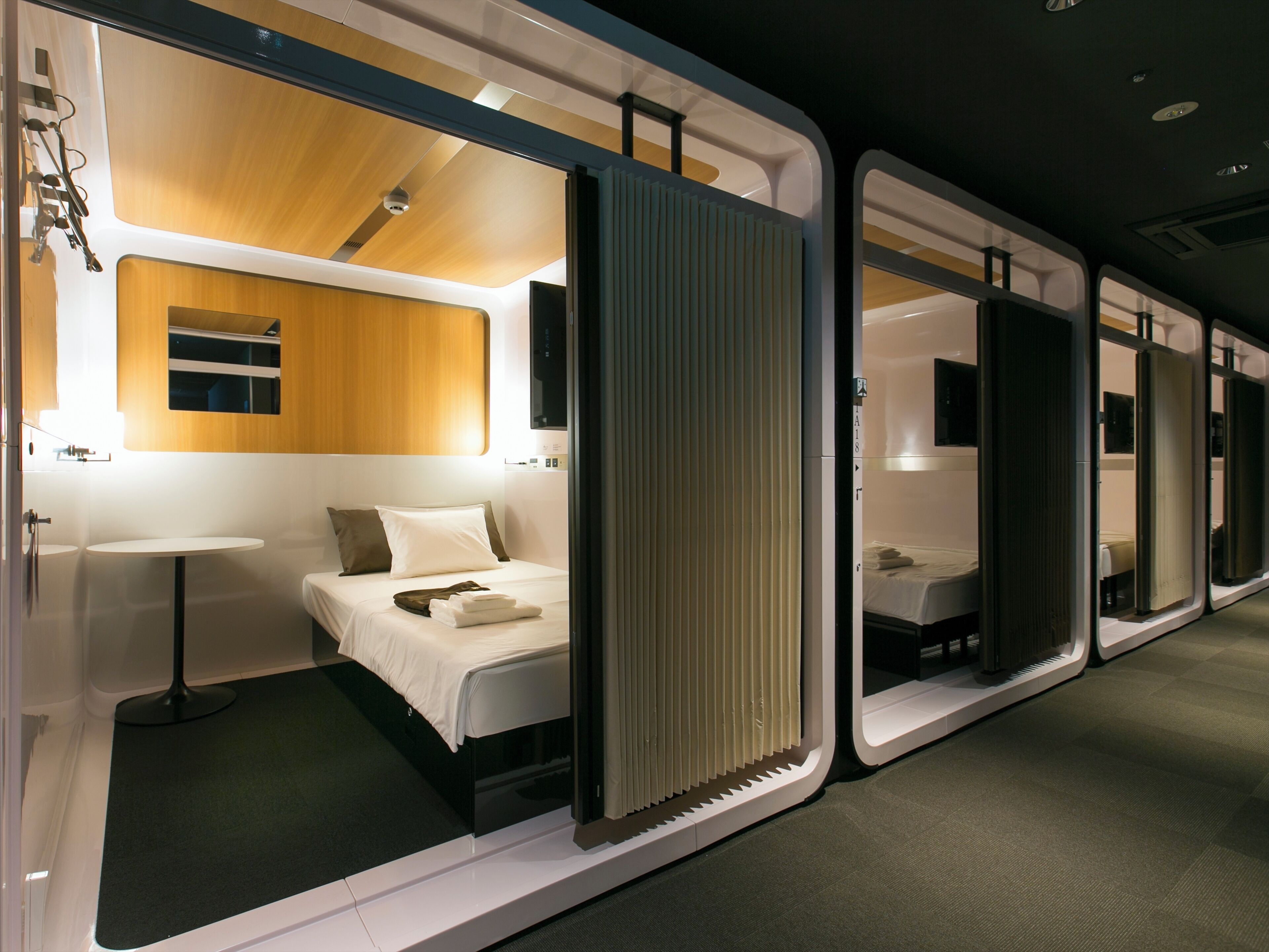 A modern hotel room with a bed, bedside table, and a view of the corridor.