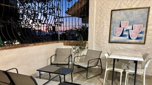 An outdoor patio area with a table and chairs, a painting on the wall, and a view of the sunset.