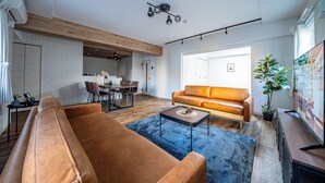 Una sala de estar moderna con un sofá de cuero marrón, un tapete azul y un comedor con mesa y sillas de madera.
