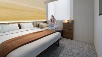 A modern hotel room with a large bed, a wooden headboard, a small seating area, and a nightstand with a lamp.