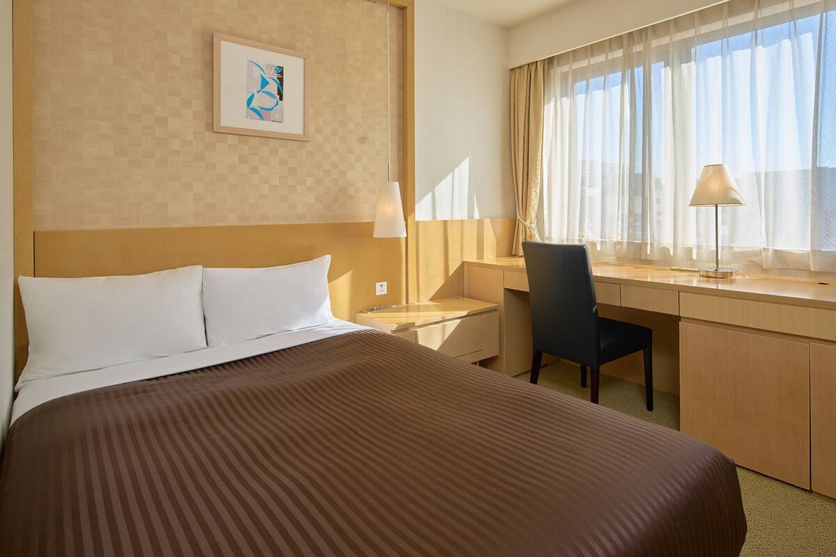 A hotel room with a large bed, a desk, a chair, and a window with curtains.