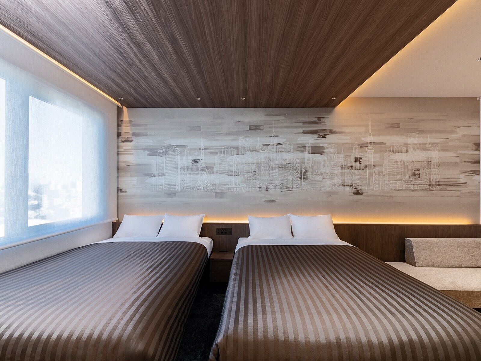 A hotel room with two beds, a cityscape mural on the wall, and a large window providing a view.
