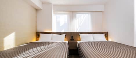 A hotel room with two single beds, a nightstand, a bedside table, and a window with blinds.