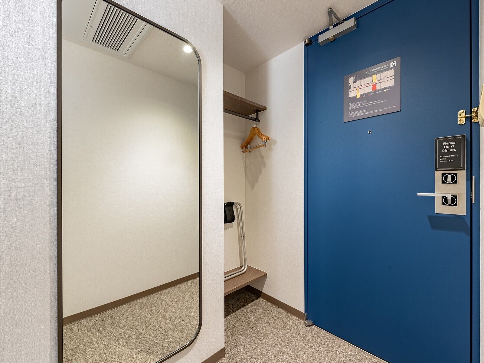 A hotel room with a blue door, a mirror, a coat rack, and a sign instructing not to disturb.