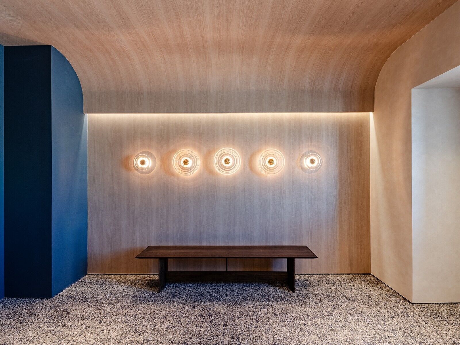A modern interior with a wooden ceiling, a bench, and illuminated wall panels.