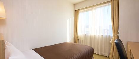 A hotel room with a bed, a desk, a chair, and a window with curtains.