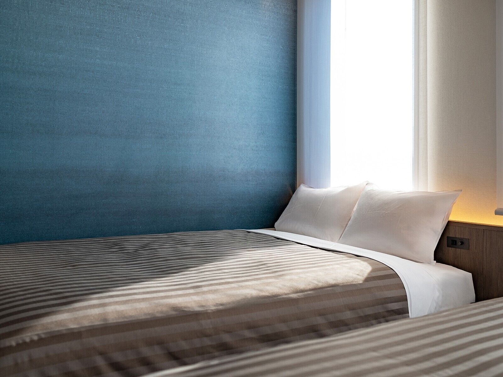 Una habitación de hotel moderna con una cama grande, una mesita de noche y un ventanal con cortinas.