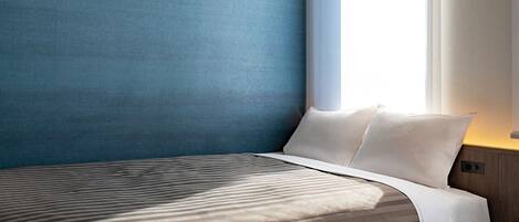 Una habitación de hotel moderna con una cama grande, una mesita de noche y un ventanal con cortinas.