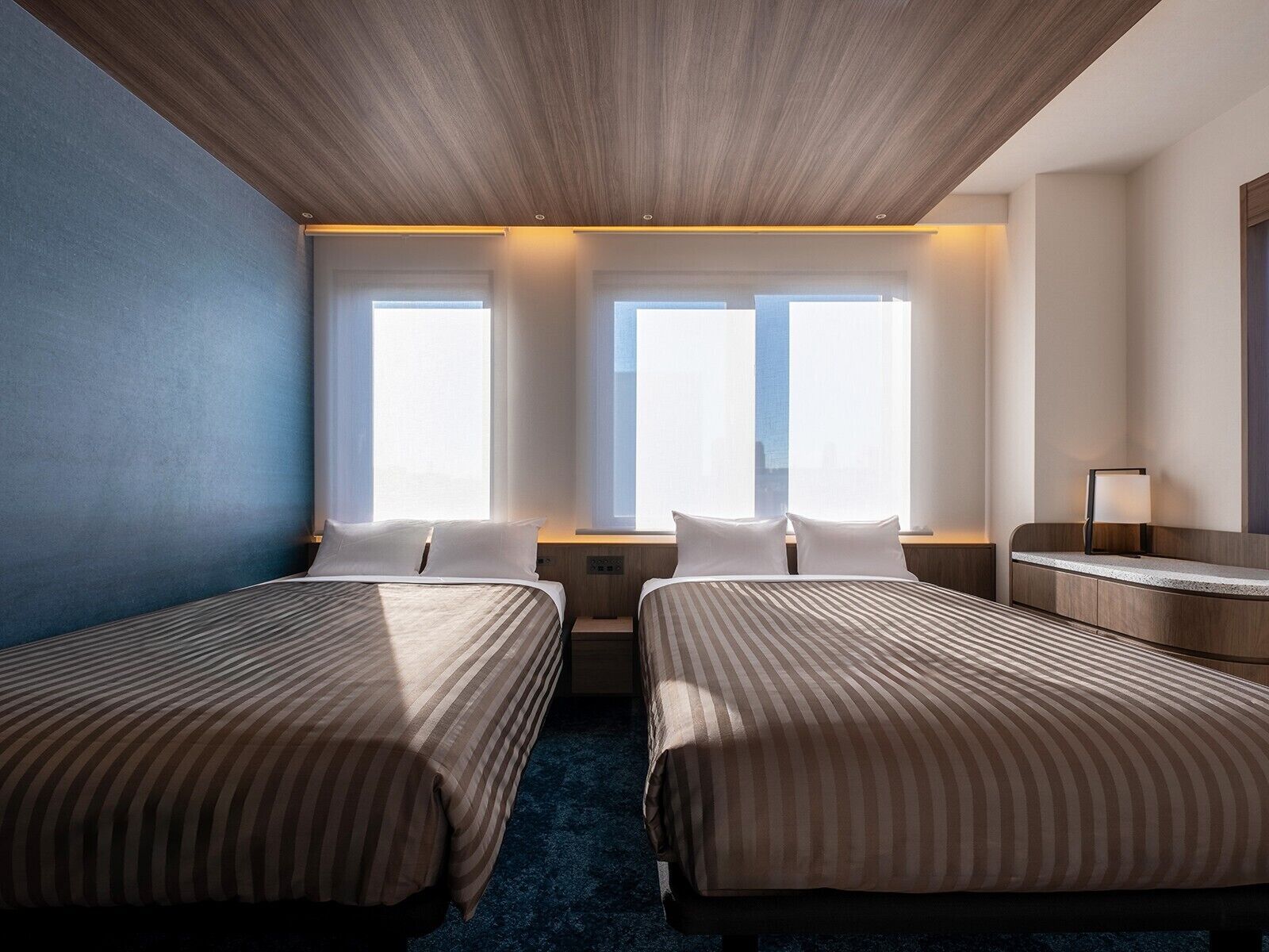 A hotel room with two beds, a desk, and a window with curtains.