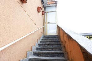 Eine Treppe führt zu einer Tür mit Glasschiebeelement, einer Handläufe und einer Wandleuchte.