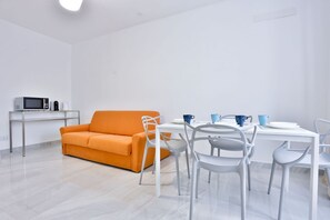 Ein heller Raum mit einem weißen Tisch, einem weißen Sofa und einer Mikrowelle auf einem kleinen Tisch.