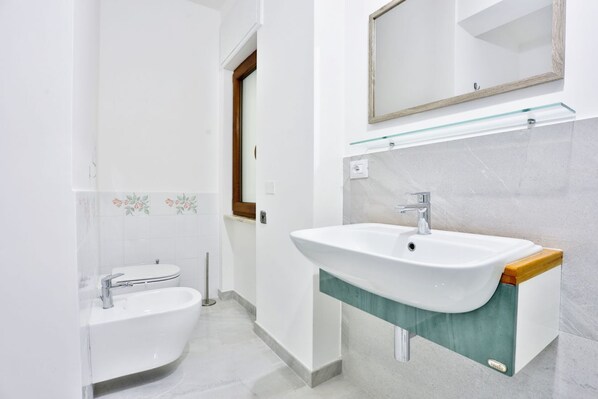 Un baño moderno con un lavamanos blanco, un estante de vidrio encima y un espejo con marco de madera.