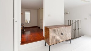 Un pasillo con piso de madera, pared blanca y baranda de metal.