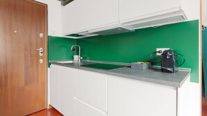 Una cocina con armarios blancos, salpicadero verde, puerta de madera y una cafetera sobre la encimera.