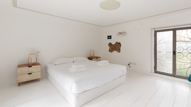 Un dormitorio con cama, mesitas de noche, una lámpara de pared y una ventana con vistas decorativas.