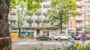 Un immeuble résidentiel à plusieurs étages, doté de balcons, situé dans une rue bordée d’arbres, avec des voitures garées.