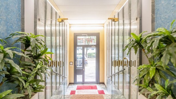 Un couloir avec des portes vitrées, une moquette rouge et des plantes en pot.