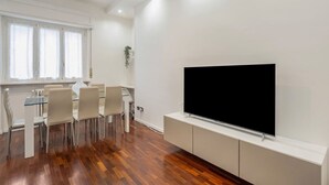 Un salon moderne doté d’un téléviseur à écran plat, d’un coin repas avec des chaises et d’une plante.
