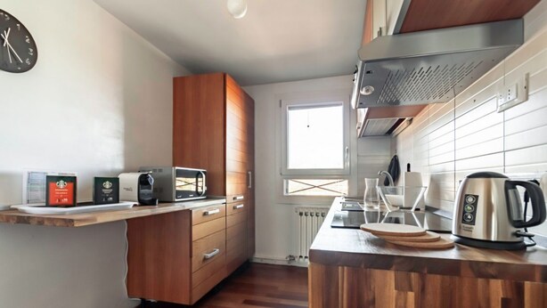 Een moderne keuken met houten kastjes, een ingebouwde magnetron, een waterkoker en een raam dat natuurlijk licht binnenlaat.