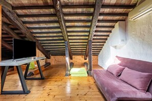Un dormitorio tipo loft con techo de madera, un sofá morado, un televisor de pantalla plana sobre un soporte y una toalla verde en el suelo.