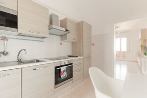 A modern kitchen with a stainless steel sink, oven, and a white chair.
