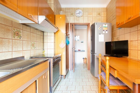 Una cocina con gabinetes de madera, una estufa de acero inoxidable, un refrigerador y un televisor.