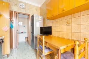 A compact kitchen with a wooden table, a TV, and a refrigerator.