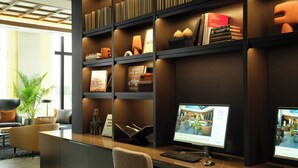 A modern reception desk with two computer monitors, a keyboard, and a mouse. There are books and decorative items on the shelves behind the desk. - AC Hotel by Marriott Detroit at the Bonstelle (Detroit)