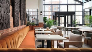 A modern interior with a long orange bench, white tables, and green chairs. - AC Hotel by Marriott Detroit at the Bonstelle (Detroit)