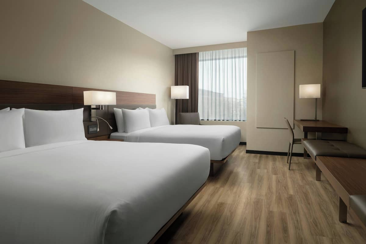 A hotel room with two beds, a desk, and a chair.