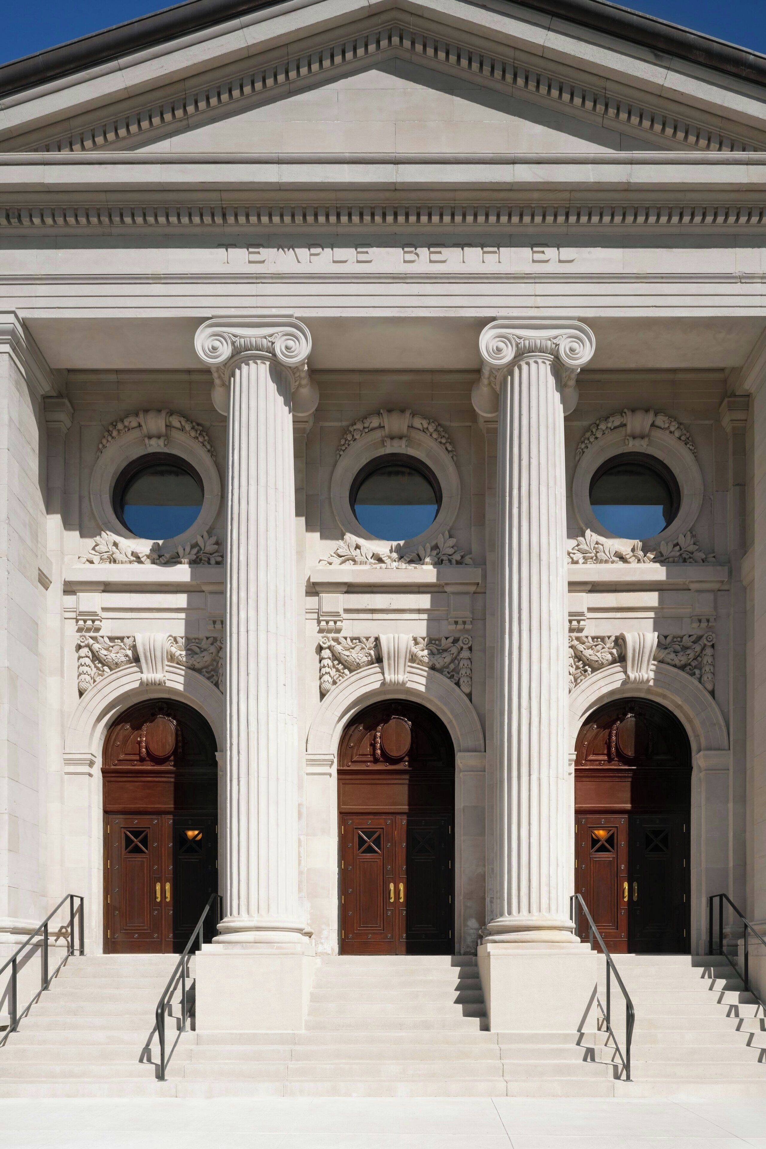 A classical building facade with three large wooden doors, a central column, and a triangular pediment with the inscription "TEMPLE BETH EL".