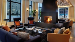 A modern hotel lobby with a fireplace, comfortable seating, and large windows offering city views. - AC Hotel by Marriott Detroit at the Bonstelle (Detroit)