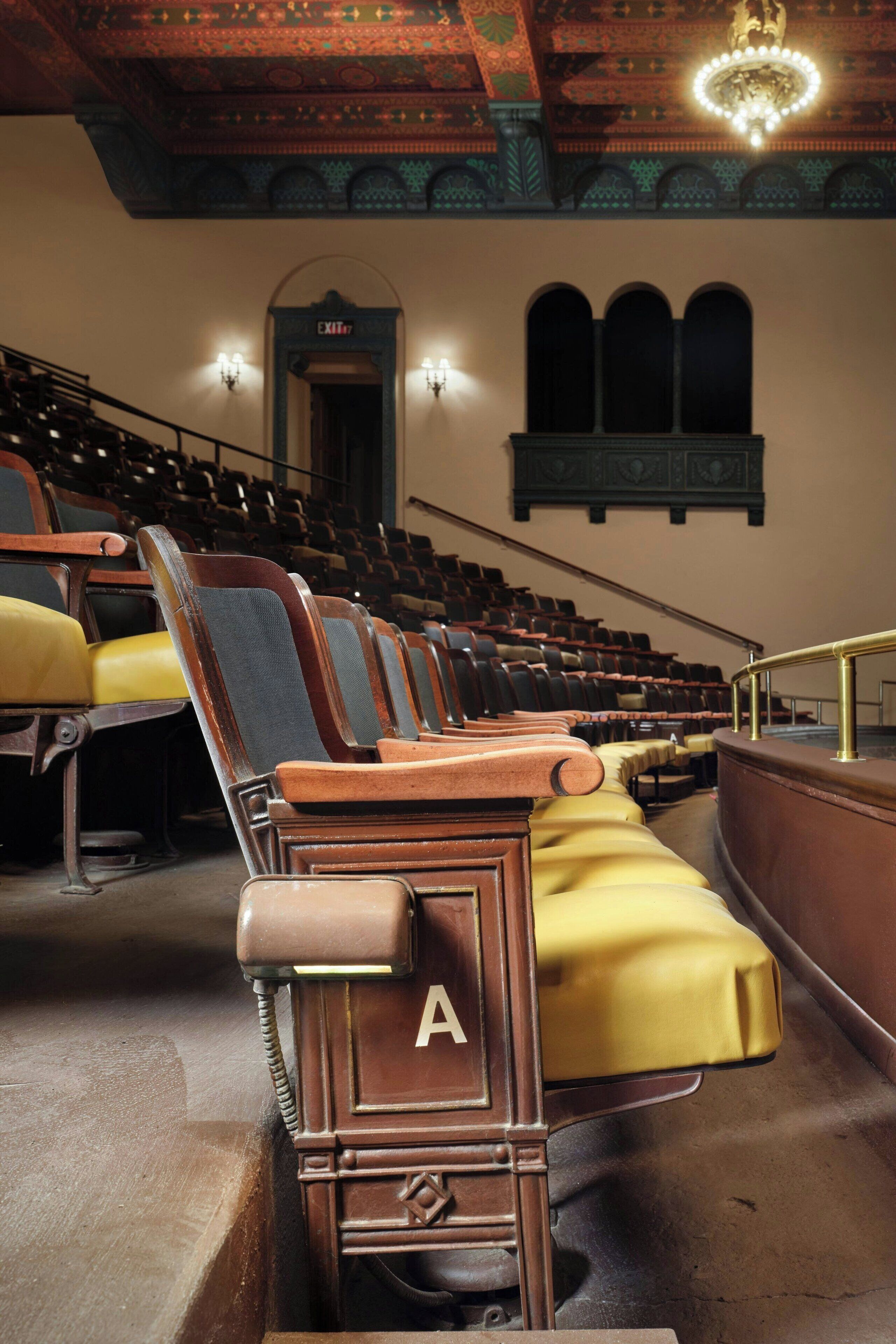 A theater with rows of wooden seats, a stage entrance, and a chandelier.