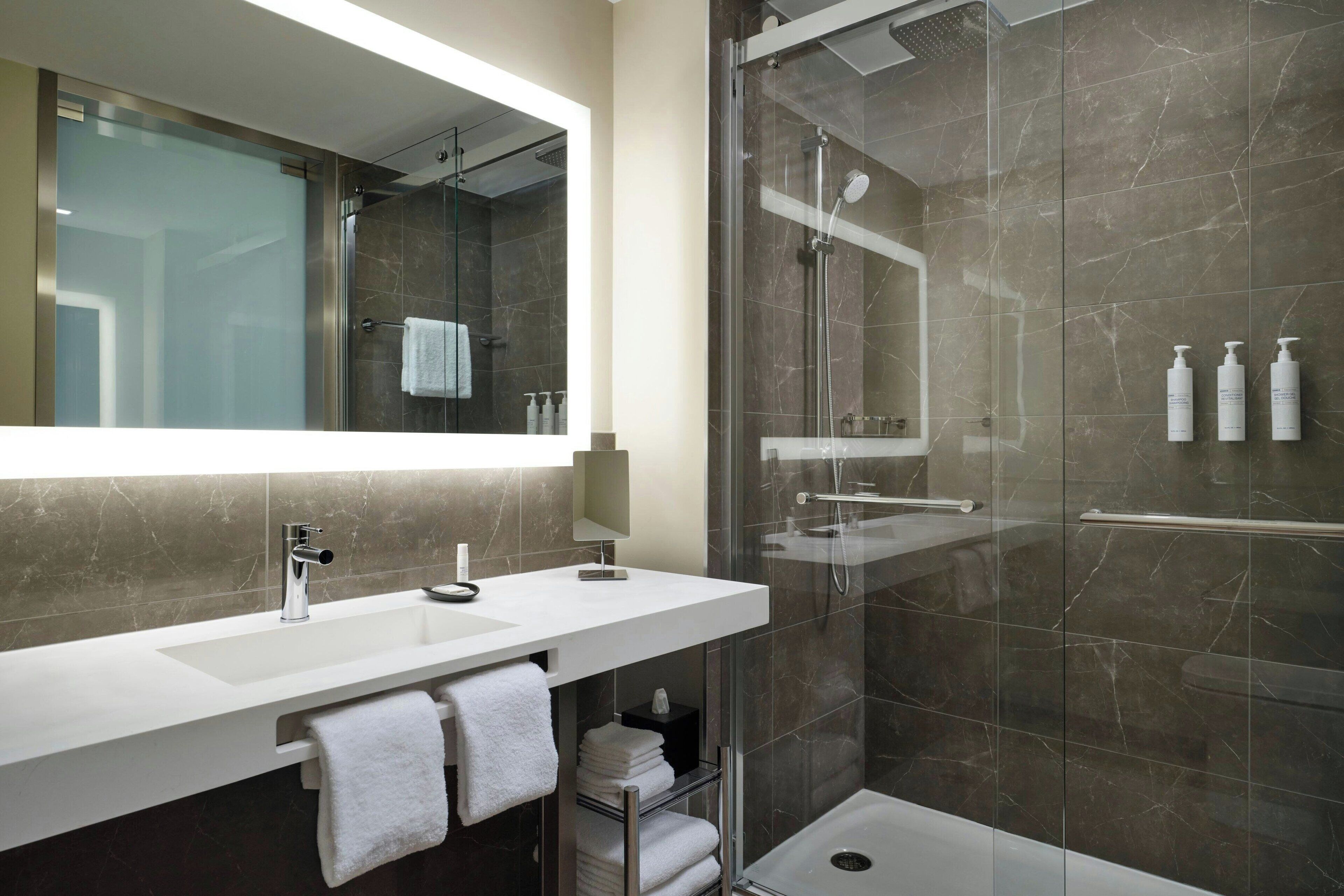 A modern bathroom with a glass-enclosed shower, a white sink, and a large mirror.