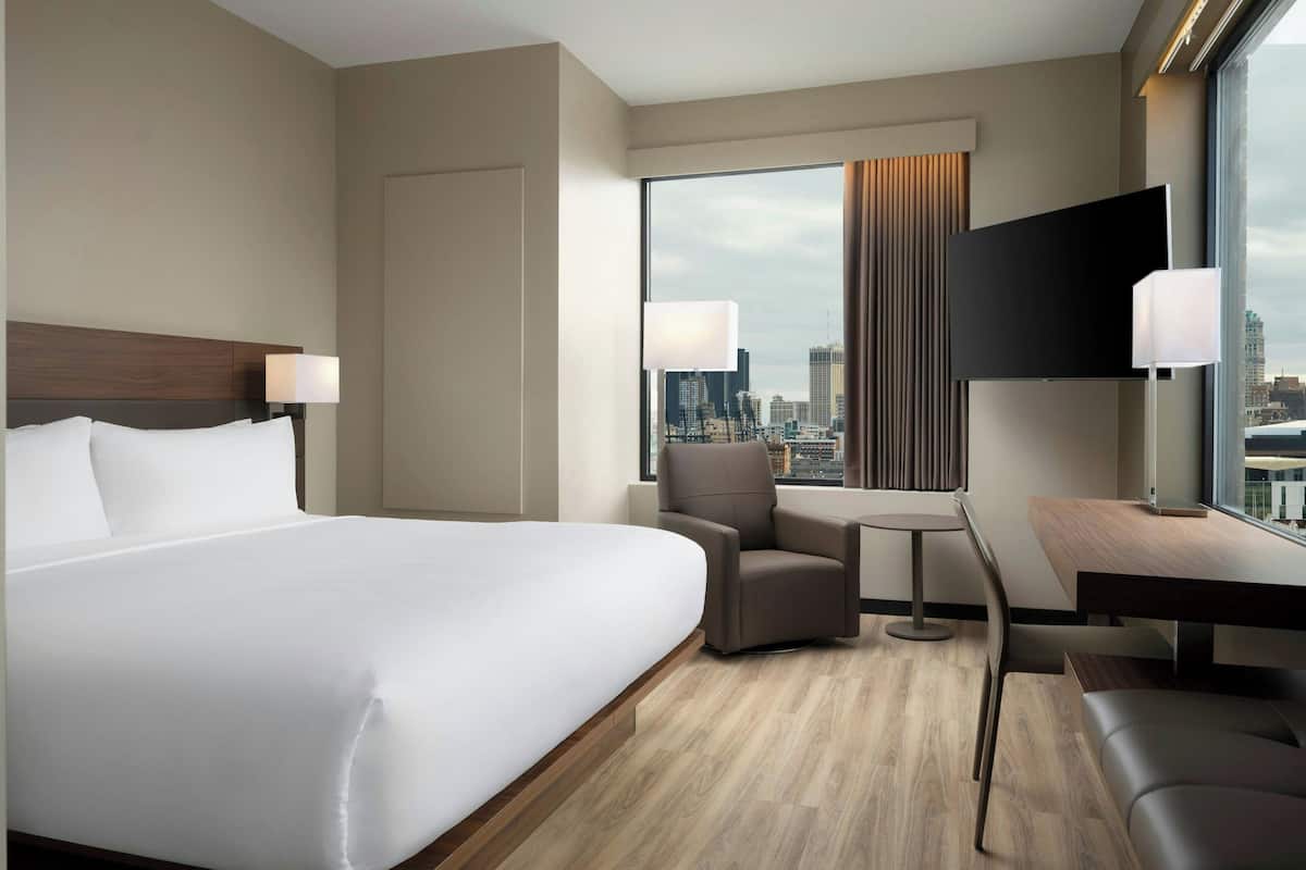 A hotel room with a large bed, a desk, a chair, and a TV.