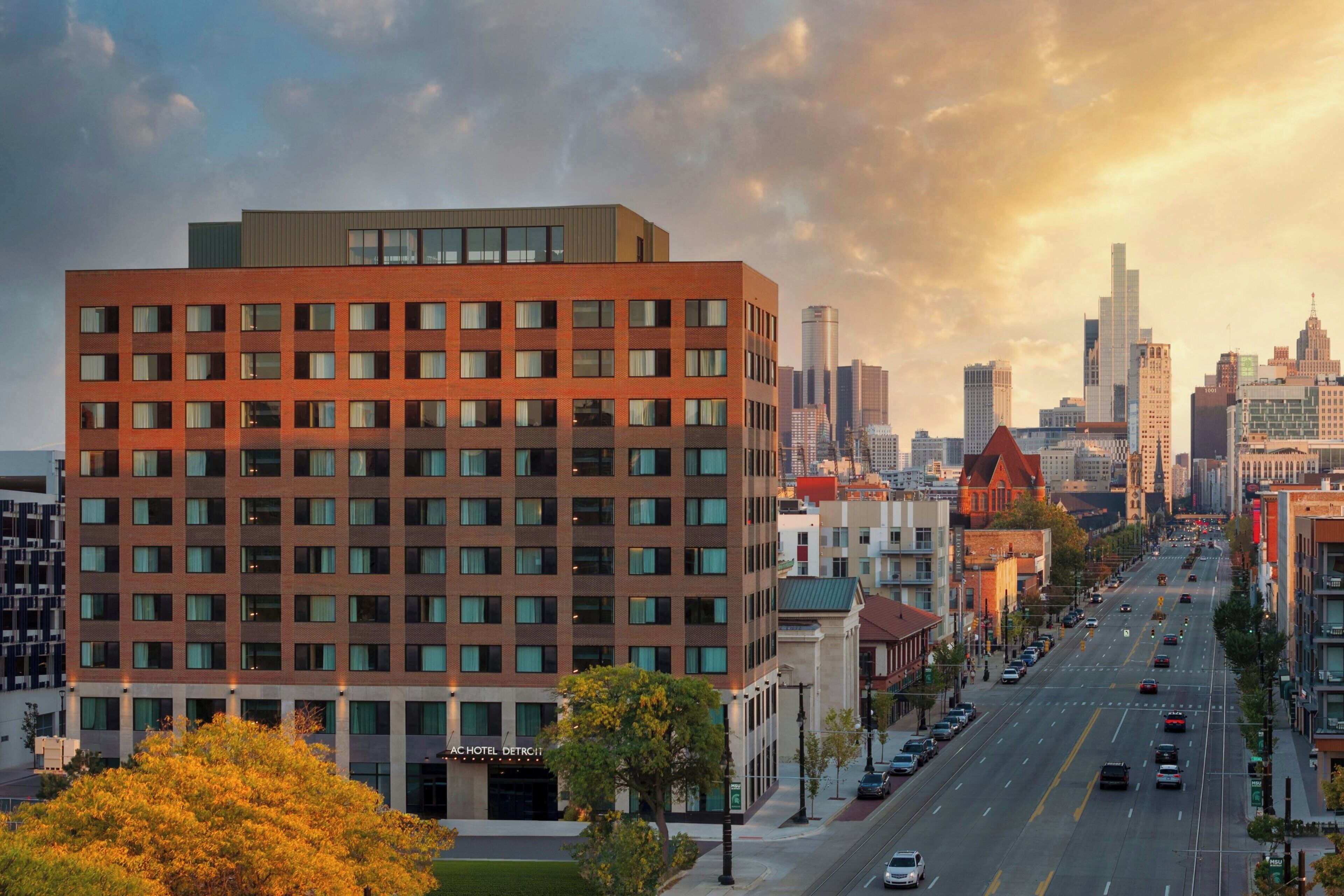 A multi-story hotel with a modern brick facade, located on a city street with a clear view of the downtown skyline.