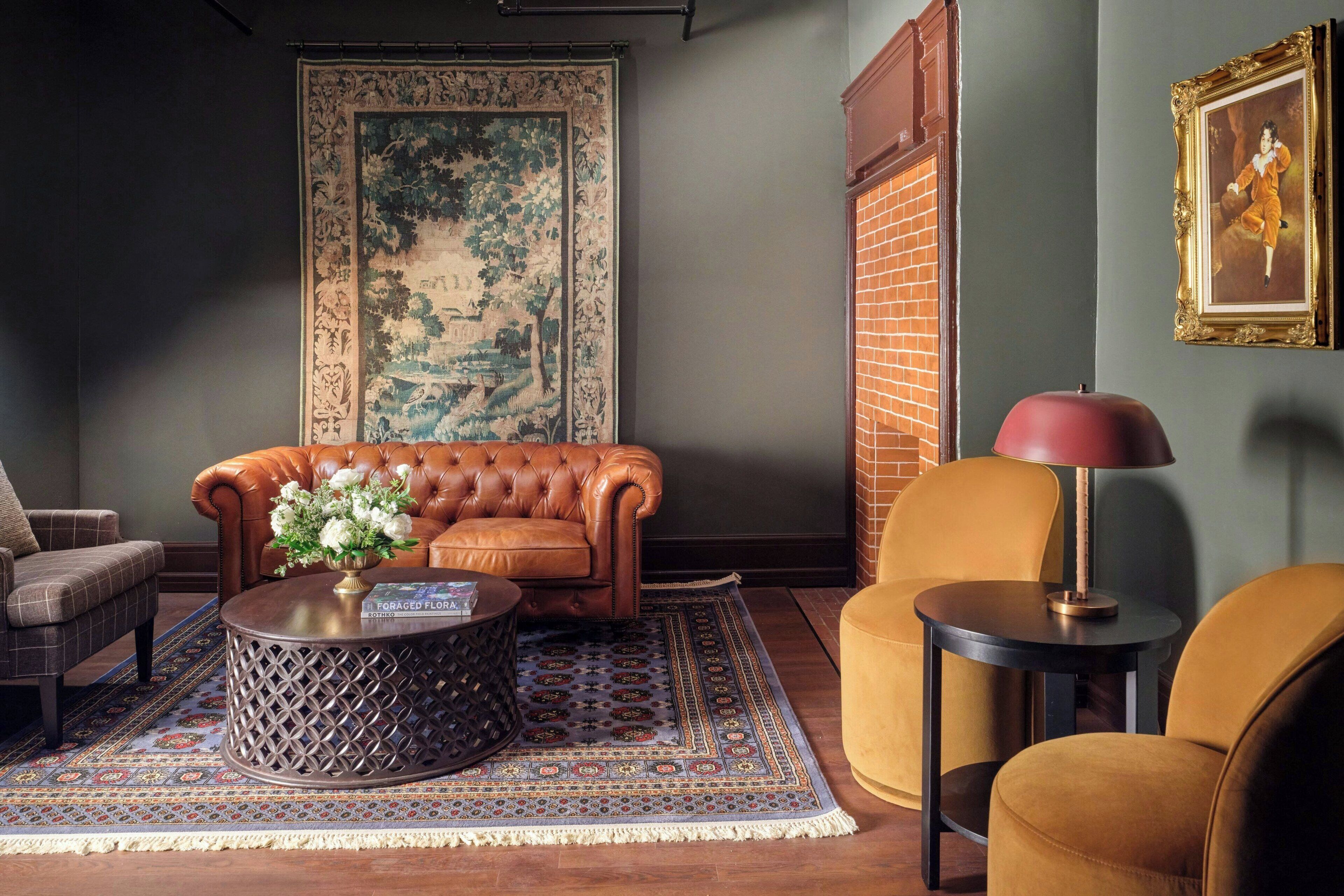 A living room with a brown leather sofa, a round coffee table with a vase of flowers, a patterned rug, and a framed picture on the wall.