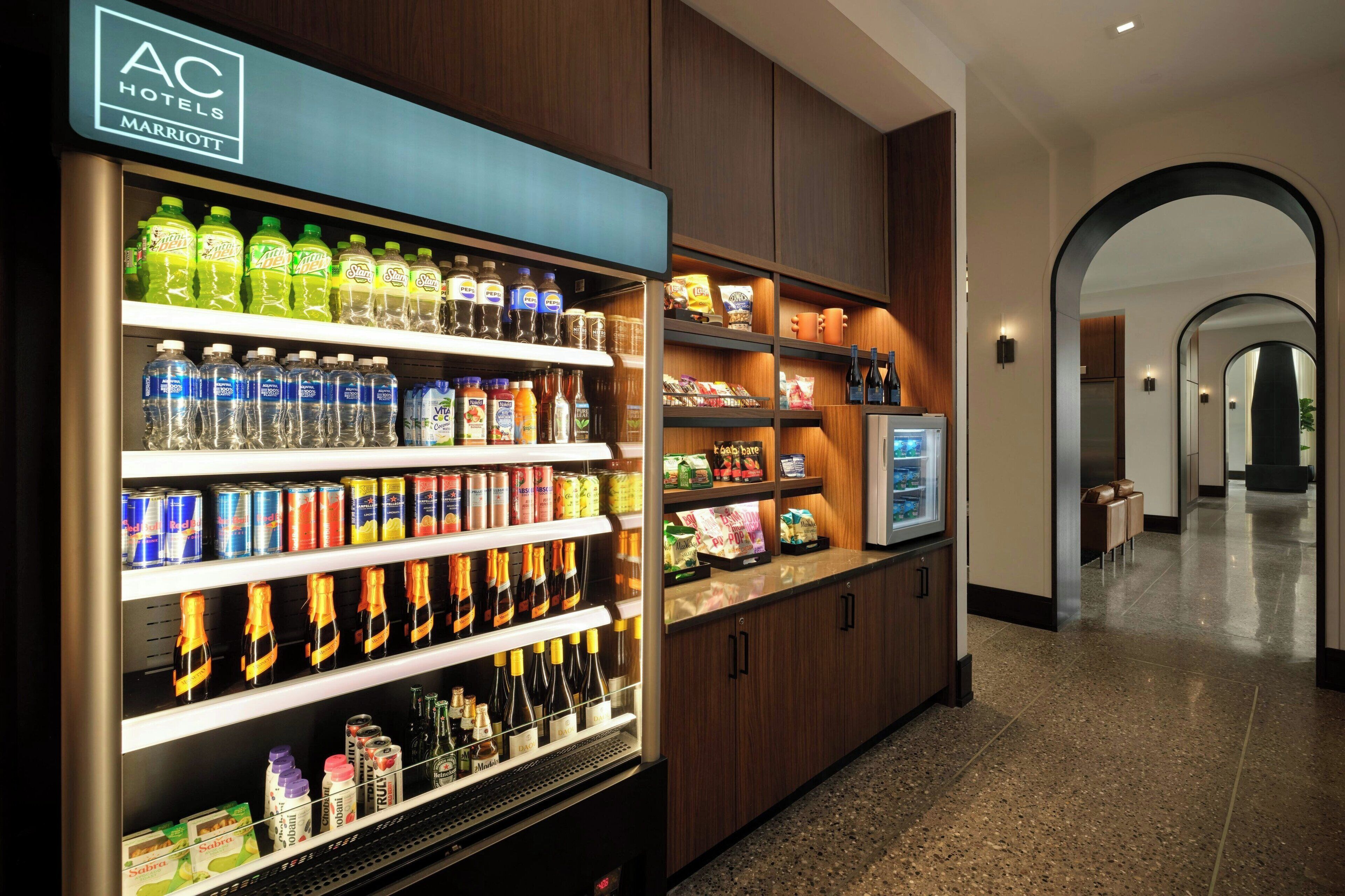 A hotel refreshment area with a self-service beverage dispenser stocked with various drinks, snacks, and condiments.