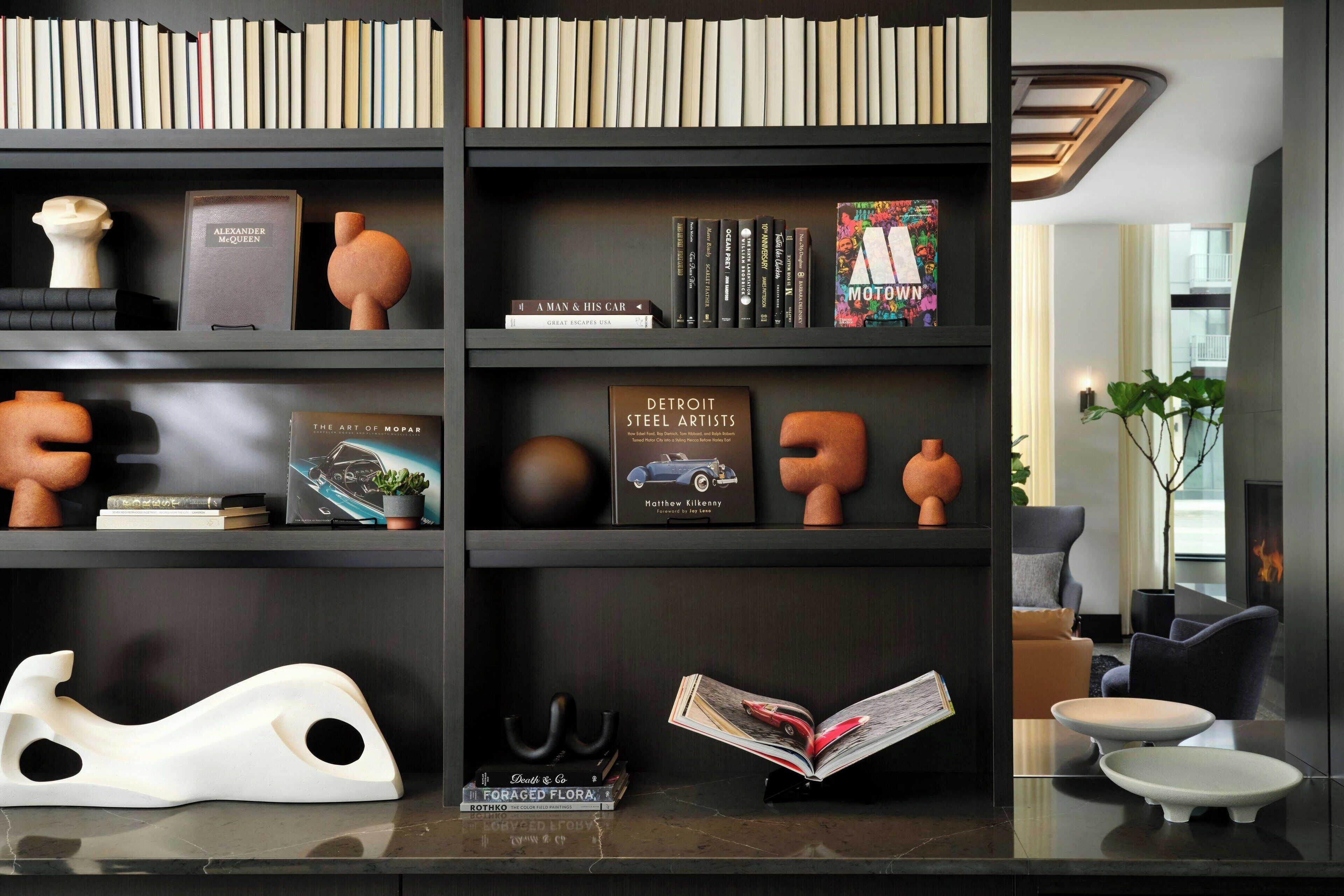 Un interior moderno con una estantería llena de libros y objetos decorativos, una escultura blanca y una chimenea.