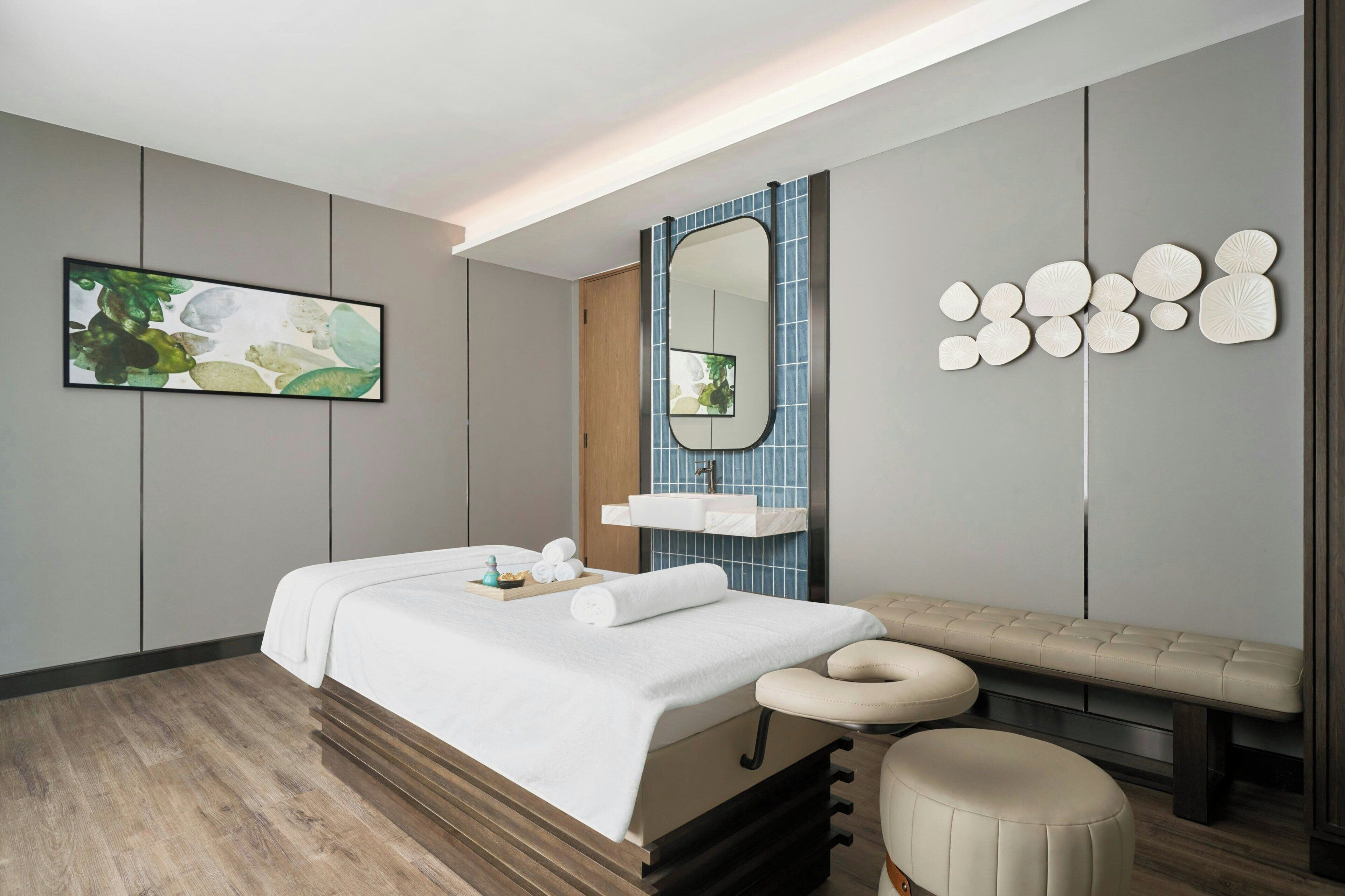 Ein modernes Schlafzimmer mit einem Bett, einer Bank, einem Spiegel und einem an der Wand befestigten Regal mit Pflegeprodukten.