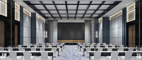 Un salón de conferencias con filas de sillas blancas, una pantalla grande al frente y una alfombra estampada.