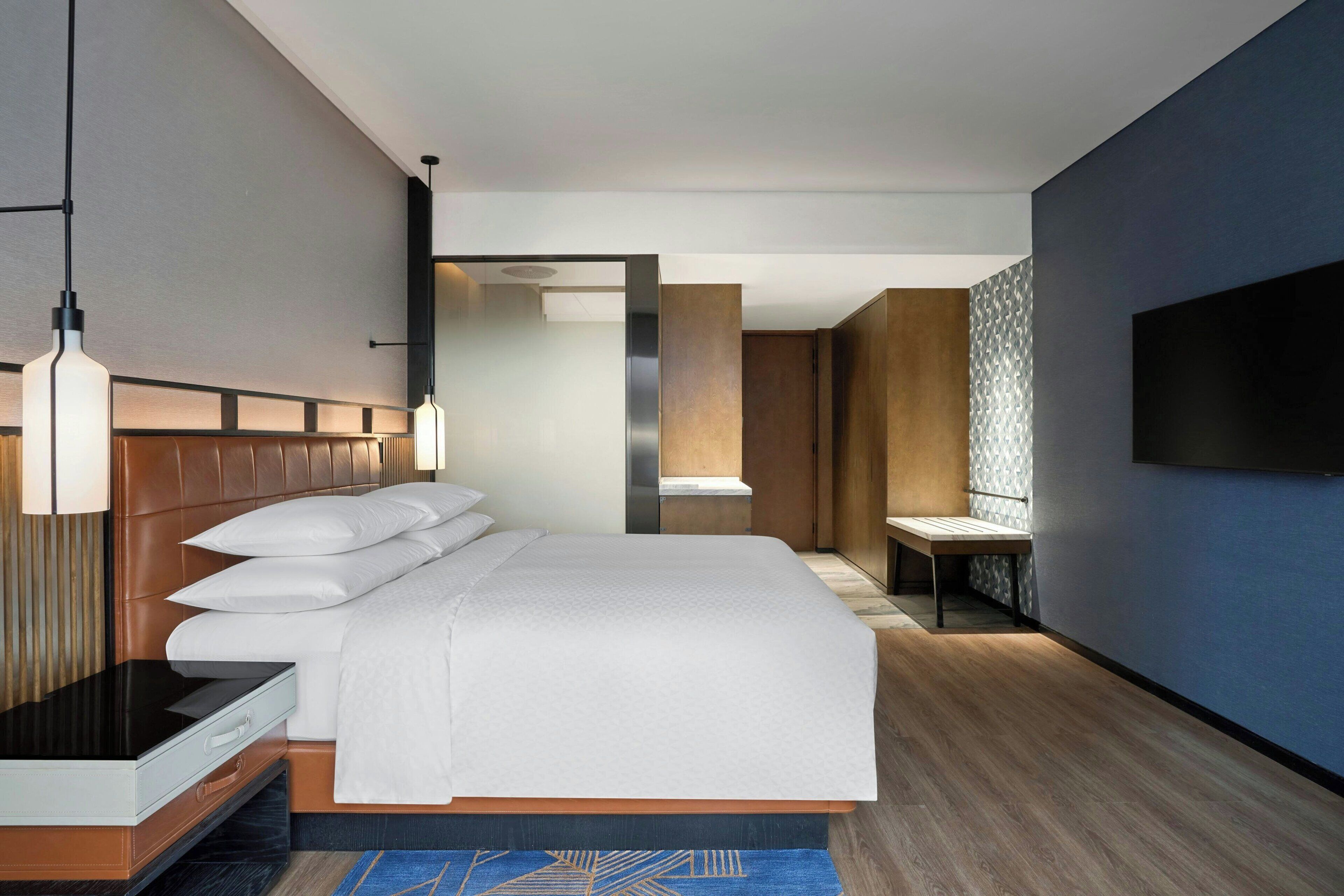 A modern hotel room with a large bed, a bedside table, a TV mounted on the wall, and a mirror.