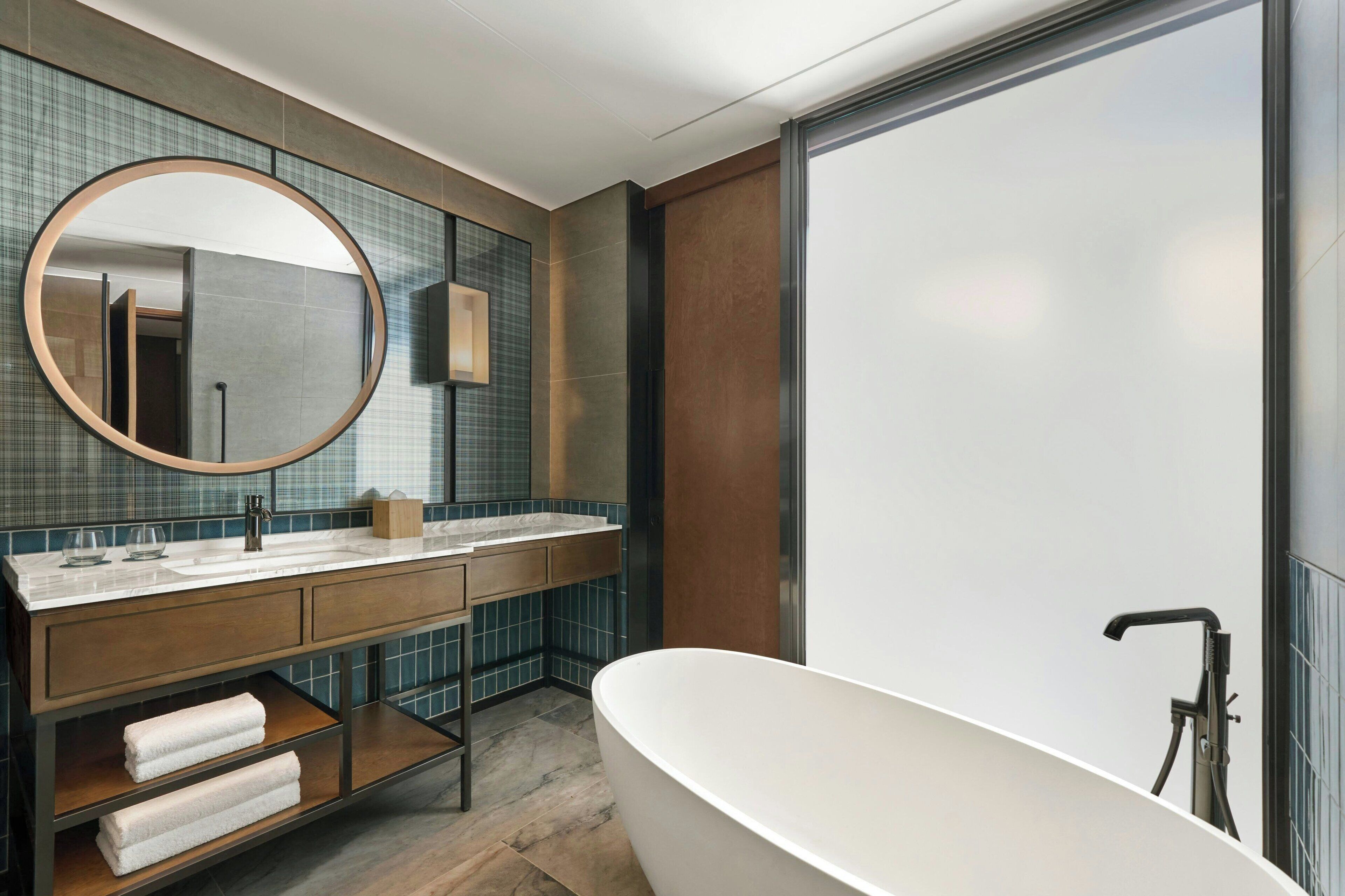 Een moderne badkamer met een vrijstaand bad, een grote spiegel en een wastafel met een betegelde spatwand.