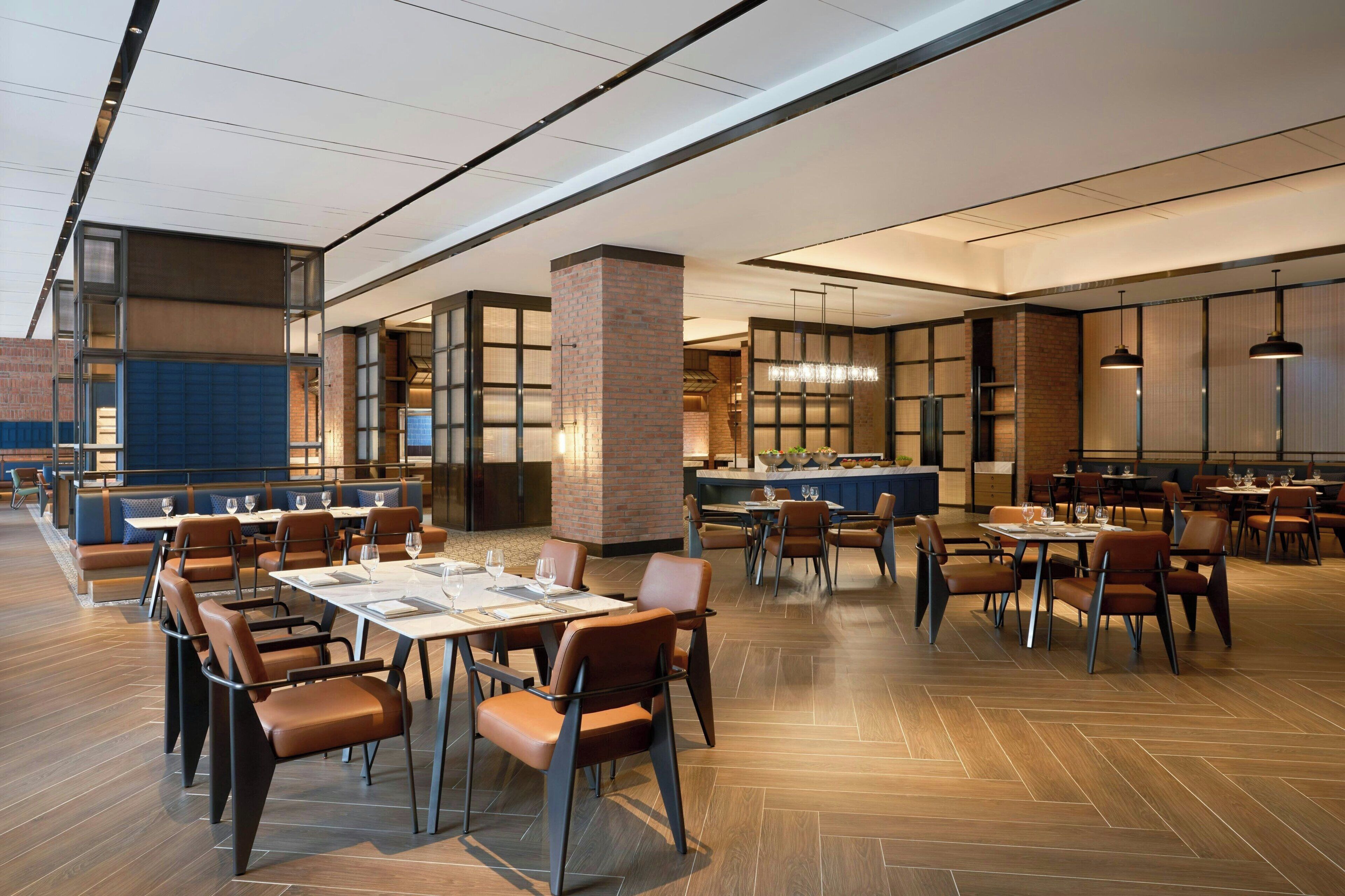 Un restaurante espacioso con mesas altas, cabinas y un columnario de ladrillo, con una lámpara moderna.
