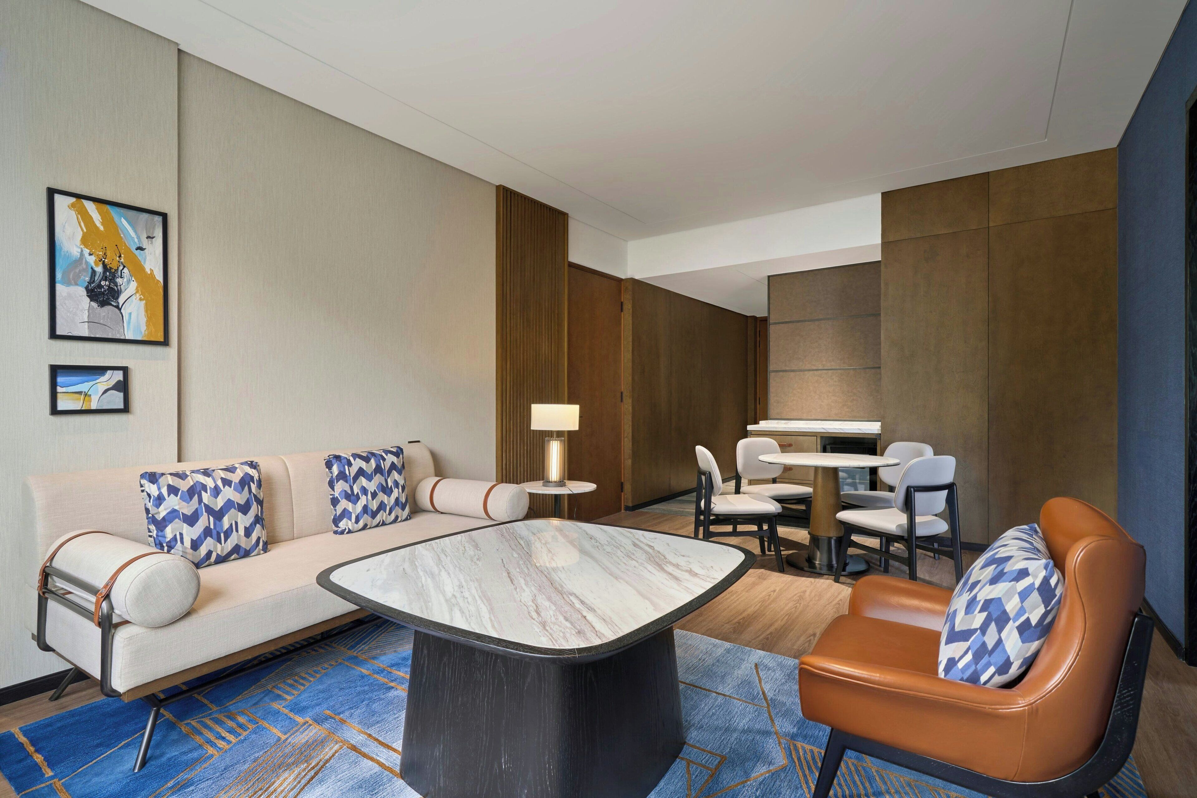 A hotel room with a sofa, armchair, dining table, and chairs.