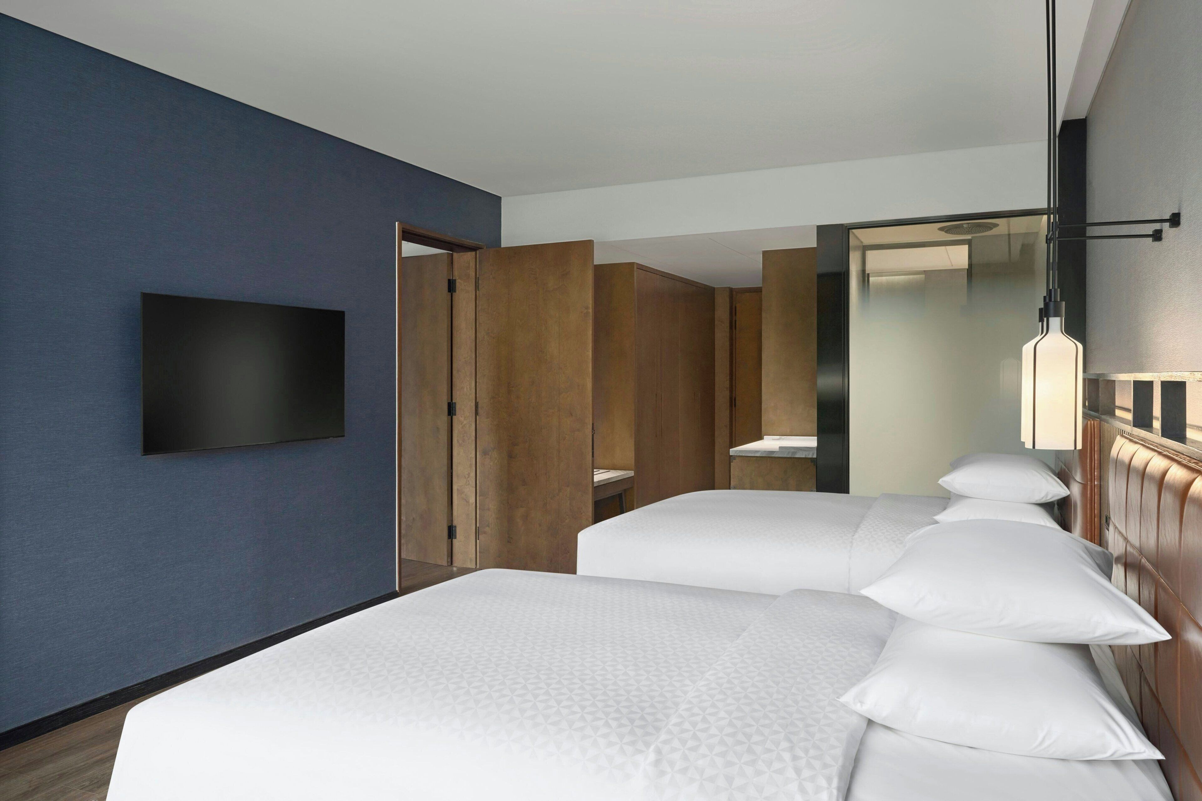 Een hotelkamer met een groot bed, een aan de muur bevestigde televisie, houten lambrisering en een spiegel.